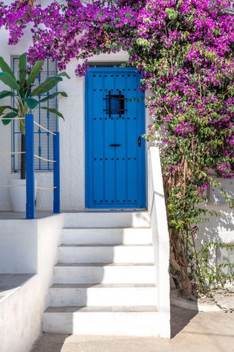 A vibrant blue door and white staircase adorned with purple bougainvillea in a Mediterranean setting.