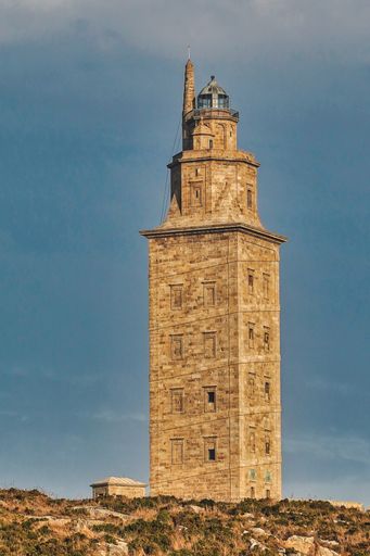 A vertical shot of Tower of Hercules in A Coruna, Galicia, Spain with a cloudy blue sky in the background