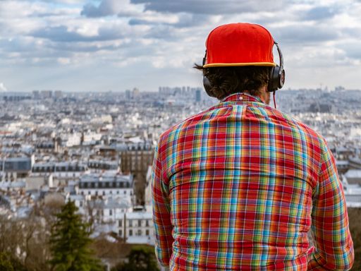 A man wearing a red cap and headphones, overlooking the cityscape of Paris from a high vantage point.