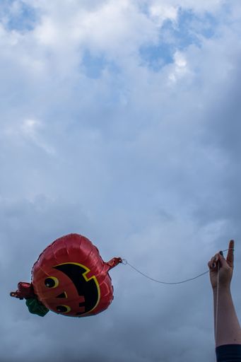 A vertical shot of a person holding a pumpkin-shaped balloon against a cloudy blue sky