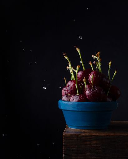 A vertical shot of a bowl full of fresh ripe cherries with water droplets on a wooden surface