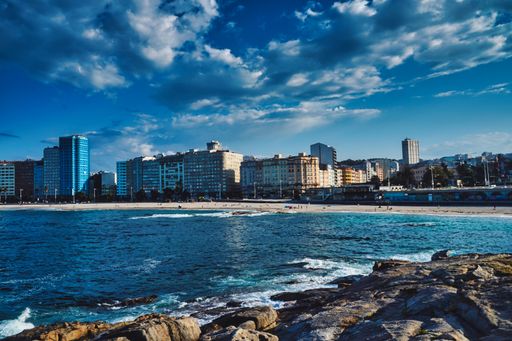 A beautiful shot of buildings and rocks on the seashore in A Coruna city in Galicia, Spain with a cloudy blue sky in the background