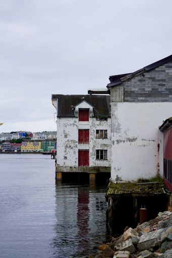 A vertical shot of the abandoned buildings along the shore of Goma in the port of Kristiansund, Norway, on a cloudy day