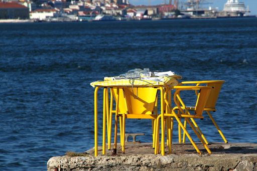 A bright yellow outdoor cafe table and chairs by the water with a cityscape background