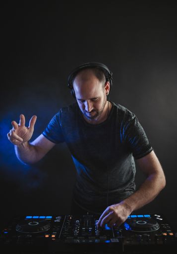 A vertical picture of a male DJ working under the blue lights in a studio