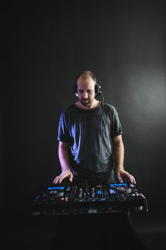 A vertical picture of a male DJ working under the lights against a dark background