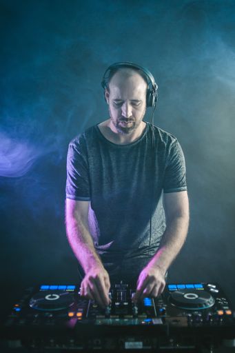 A vertical picture of a Male DJ under the blue lights and smoke in a studio