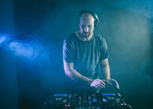 A male DJ working under the blue lights and smoke in a studio against a dark background