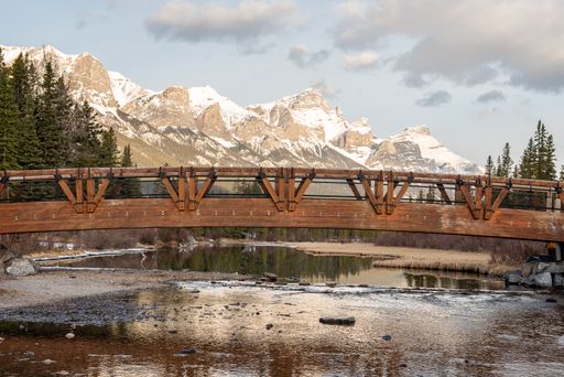 The wooden bridge in Policeman's Creek in Canmore during early spring with snowy peaks in the background