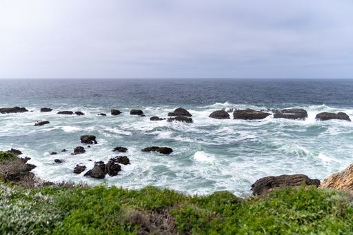 A scenic view of the rocky coastline with waves crashing against the rocks under a cloudy sky