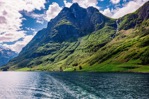 A stunning view of a lush green mountain with a clear blue sky and a calm lake in the foreground.