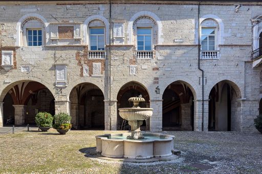 A historic courtyard with an ornate stone fountain and arched windows in Brescia, Italy