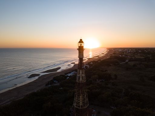 An aerial shot of a beautiful orange sunset over the beach with a lighthouse