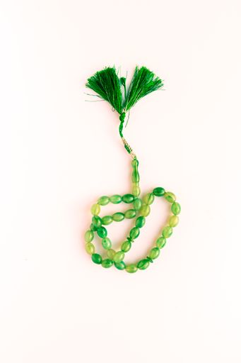 A vertical shot of a green rosary on a white background