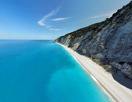 Aerial view of a pristine beach with turquoise water and a rugged cliffside under a clear blue sky in Lefkada, Greece