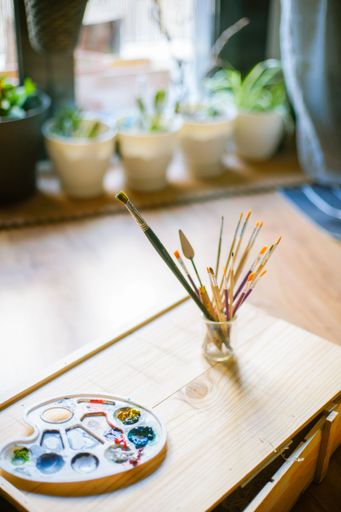 An artist's workspace with a palette of paints and brushes in a jar