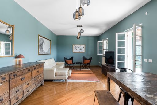 Modern living room with teal walls, wooden furniture, and a cozy seating area featuring a white sofa and butterfly chairs