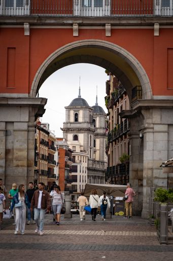 The people walk through an archway in Plaza Mayor with a view of Almudena Cathedral in Madrid, Spain