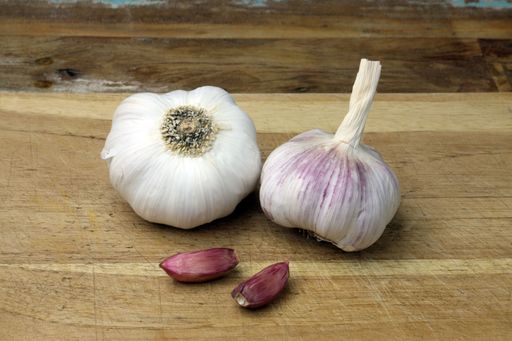 A close-up of two whole garlic bulbs and two garlic cloves on a wooden cutting board
