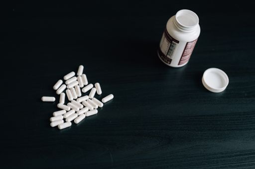A high-angle shot of many pills and a container on a wooden table