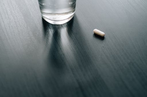 A closeup shot of a white capsule near a glass of water on a wooden surface