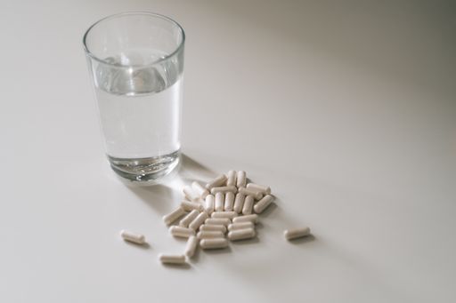 A high-angle shot of many pills and a cup of water on a white table