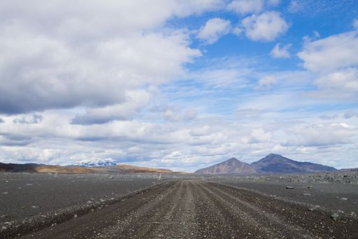 A scenic view of a gravel road leading to distant mountains under a partly cloudy sky.