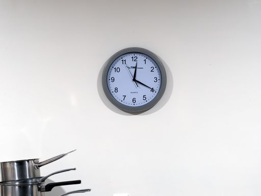 View of round clock on kitchen wall with pile of saucepans in corner. Auckland, New Zealand - July 4, 2021