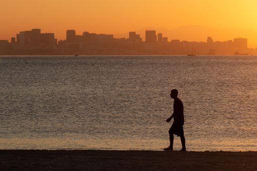 A silhouette of a person walking along the beach during sunset with a city skyline in the background