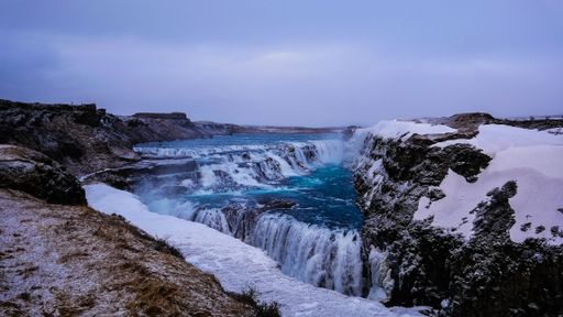 A scenic view of waterfall in Iceland during winter with snow-covered cliffs and clear blue waters