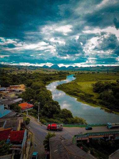 An aerial view of a river curving through a rural town with mountains in the background