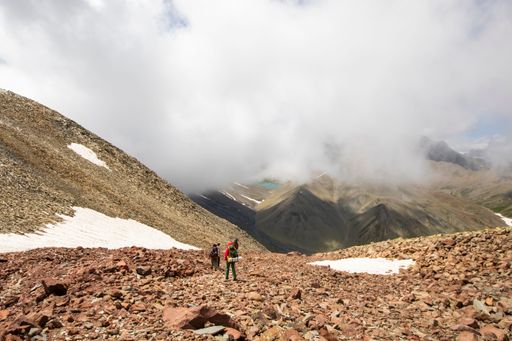 The hikers exploring a rocky mountain landscape with patches of snow and clouds enveloping the peaks