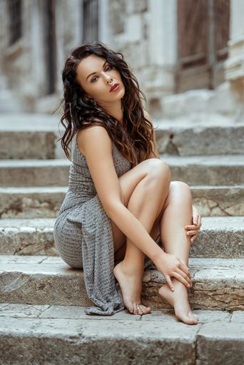 A sexy Caucasian brunette woman wearing a dress and no shoes sitting on the stairs