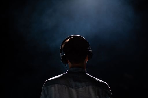 A back view of a man wearing headphones in a dark room with a spotlight illuminating him