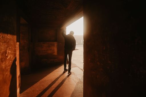 A Silhouette of a person standing in a doorway with sunlight streaming in, creating long shadows.