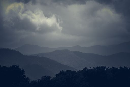 A dramatic landscape of mountains under a cloudy sky, creating a moody atmosphere