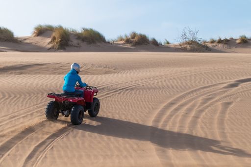 A scenic view of a person driving a red Quad Bike at the beach in Essaouira, Morocco