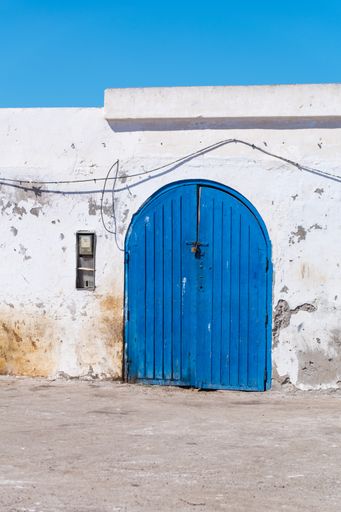 A vertical shot of an old blue door in Essaouira Harbor, Morocco