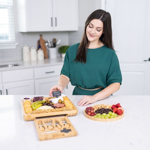A woman preparing a charcuterie board with various cheeses, fruits, and nuts in a modern kitchen