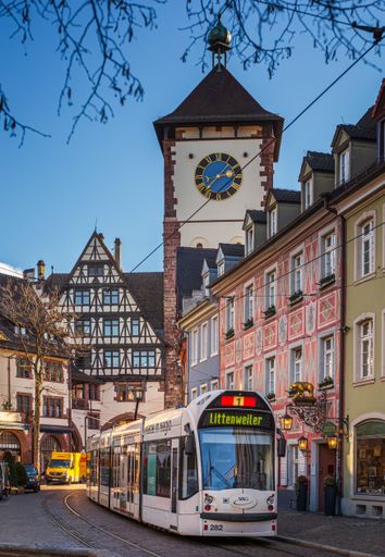 A charming street scene in Freiburg im Breisgau, Germany featuring a tram and the historic Schwabentor with a clear blue sky.