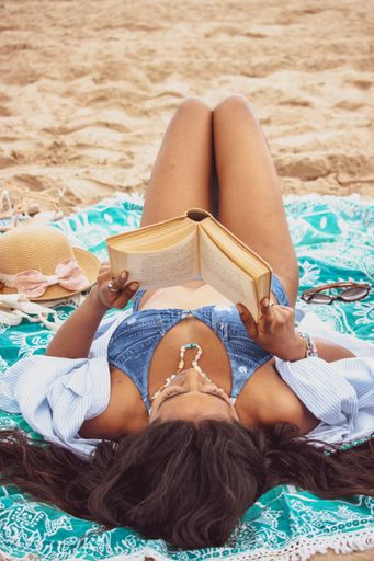 A young female lying on the sandy beach and reading a book