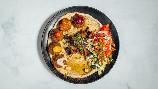 A closeup shot of a delicious meal with falafel, hummus, seasonings and vegetables