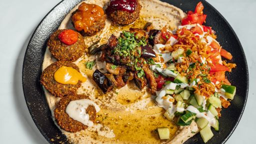 A closeup shot of a delicious meal with falafel, hummus, seasonings and vegetables