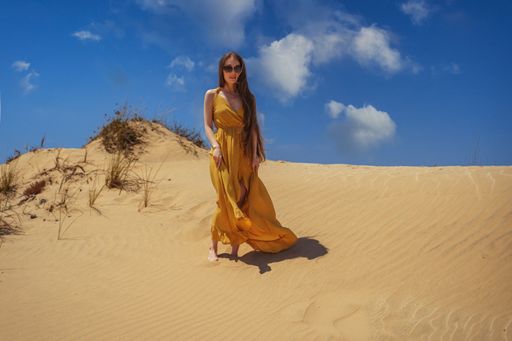 A beautiful woman with long hair and a yellow dress posing in the desert.