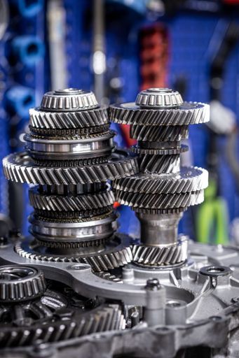 Close-up of a complex gearbox mechanism with gears and bearings in a workshop setting.