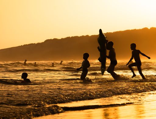 Silhouette of children playing in the sea during sunset with hills in the background.