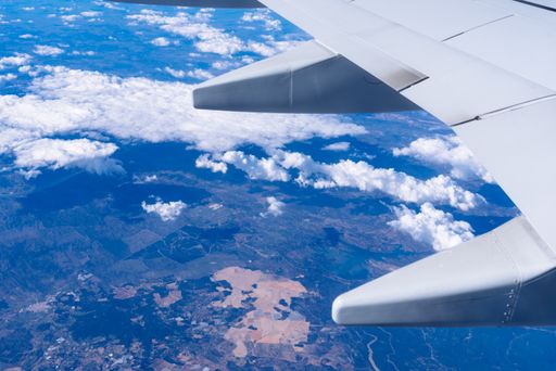 A view from an airplane window with the wing visible above white clouds hovering over land