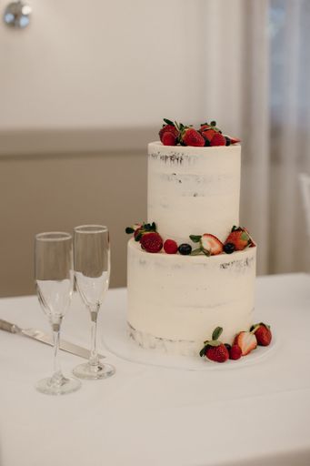 A two-tier white wedding cake with fresh strawberries and blueberries on a table