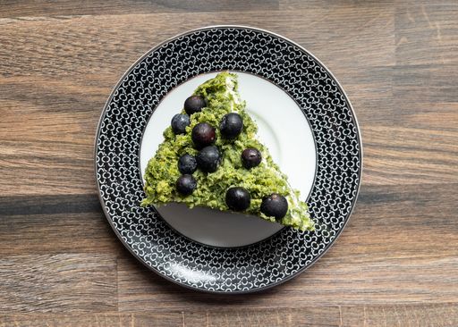 A top view of a delicious piece of matcha cake with blueberries on a plate on the table
