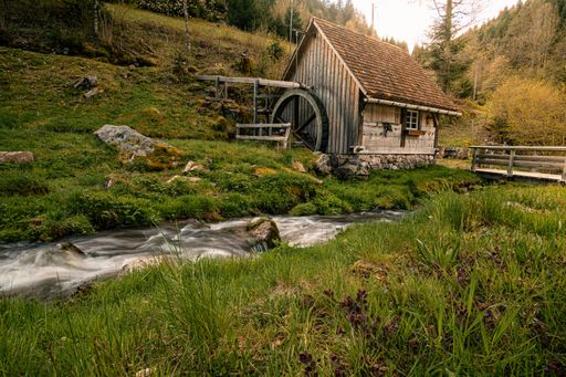 A scenic view of an old wooden house in the forest next to a small river